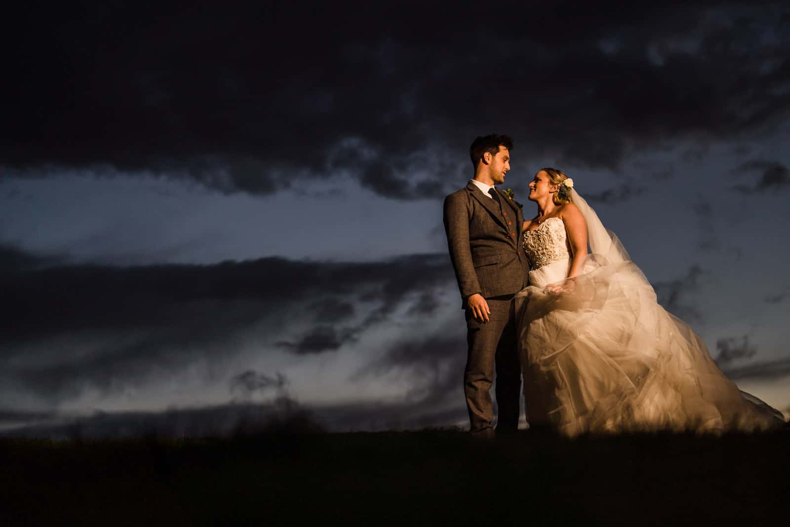 Photo of a wedding couple standing in Dodford Sheep field in evening, External flash used with magmod accessories